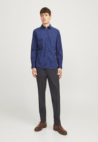 Marineblå mønstrete skjorte med knapper og et subtilt prikkedesign, kombinert med mørke bukser og brune sko, i slim fit stil.