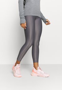 Šedé fitted legíny s plochými švy, spárované se světle růžovými teniskami s texturovaným svrškem a kontrastními akcenty.