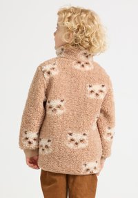 Fleece pullover in beige, featuring a soft, textured surface with a repeated cat face pattern in cream and brown. High collar and long sleeves.