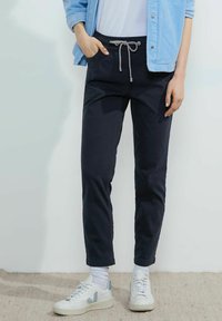 Pantalones azul marino, ajustados, con cinturilla elástica y cordón; bolsillos laterales; combinados con zapatillas blancas y una camisa azul clara.