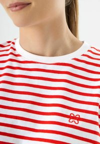 Rood en wit gestreepte t-shirt, katoenen materiaal, ronde halslijn, met een klein geborduurd bloemenontwerp aan de onderkant rechts.