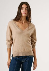 Bežna v-izrez jopica z dolgimi, zavitimi rokavi, rebrastimi manšetami in robom. Mehka tekstura, sproščen fit, kombinirana z temno modrimi koti.