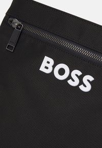 Black textured fabric with a smooth zipper. Features a prominent white "BOSS" logo in a bold font on the surface.