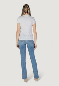 Weißes T-Shirt mit kurzen Ärmeln im klassischen Schnitt, kombiniert mit hellblauen Schlagjeans und klaren Absatzschuhen, von hinten betrachtet.