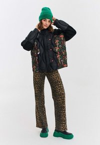 Czarna pikowana kurtka z kwiecistymi rękawami, czerwonymi guzikami, w zestawie z spodniami w panterkę i zielonymi, masywnymi trampkami. Zielona czapka beanie.