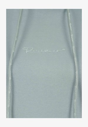 Licht saliegroen top met ribbelstructuur, voorzien van een ritssluiting en subtiel geborduurd logo op de borst. Eenvoudig en gestroomlijnd ontwerp.