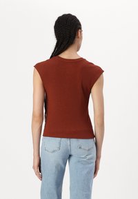 Rustfarget tettsittende tanktopp med korte ermer, ribbestrikket tekstur og rund hals, kombinert med lyseblå denimjeans.