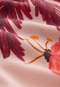 Stof met een zachte roze achtergrond en grote rode en oranje bloemenpatronen, zichtbaar geweven textuur en subtiele plooien.