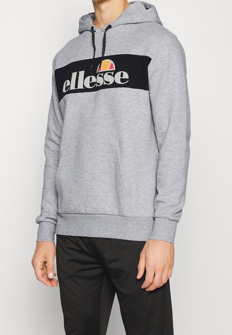 Sweat à capuche gris avec panneau avant noir arborant le logo "ellesse". Capuche ajustable avec cordon de serrage et poche kangourou. Poignets et ourlet côtelés.