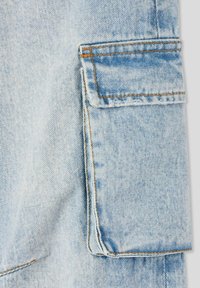 Tessuto in denim azzurro chiaro con un dettaglio della tasca ben visibile. Presenta cuciture arancioni a contrasto e una texture morbida. Finitura pulita dei bordi.