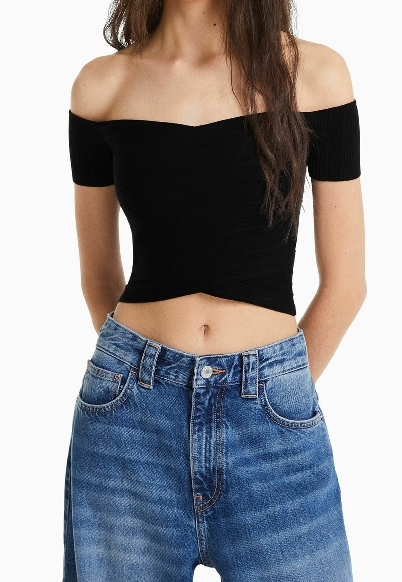 Svart ribbad off-shoulder crop top tillsammans med högmidjade ljusblå jeans. Toppen har en figurnära design och en mjuk textur.