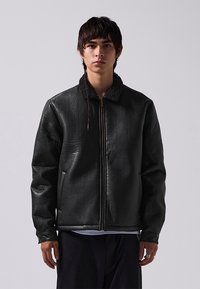 Black leather jacket with a zip front, featuring a textured collar and two side pockets. The design is boxy with padded shoulders.
