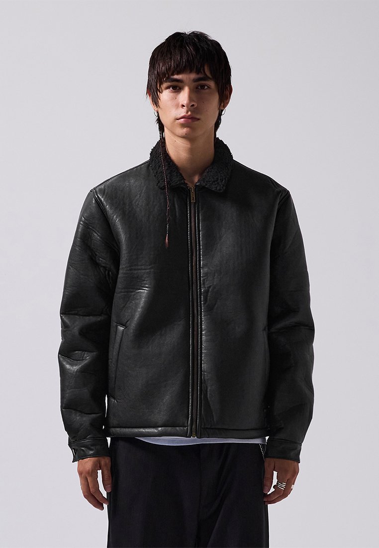 Giubbotto in pelle nera con zip frontale, dotato di un colletto testurizzato e due tasche laterali. Il design è a forma quadrata con spalline imbottite.