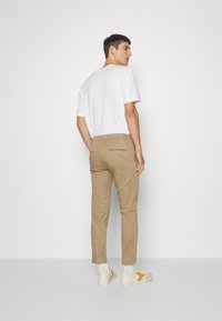 Lichtbeige broeken met een slim fit, achterzakken en nette naden, gecombineerd met een effen wit t-shirt en casual sneakers.