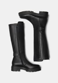 Bottes en cuir noires, montant jusqu'au genou, avec une finition mate, des fermetures éclair sur le côté et une semelle en caoutchouc épaisse. Présentent un bout arrondi et des accentuations cousues.