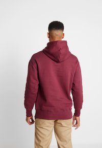 Burgundowa bluza z dużym kapturem z tyłu, ściągaczami przy rękawach i u dołu, wykonana z miękkiego materiału, o luźnym kroju i minimalistycznym designie.