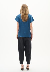 Top scurt de culoare albastră cu un croi lejer și o textură fină, asortat cu pantaloni negri tapered și sandale cu toc, văzut din spate.