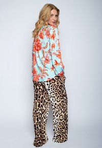 Een turquoise blouse met oranje bloemenpatronen, gecombineerd met leeuwenprint broek. De outfit heeft een comfortabele pasvorm en een zijdezachte textuur.