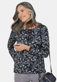 Langsleeve zwart top met een wit en grijs abstract patroon, ronde hals en een iets losse pasvorm, aangevuld met een zwarte schoudertas.