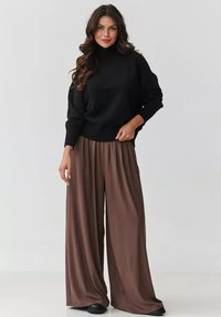 Czarny sweter z golfem z dzianiny, z prążkowanymi mankietami, zestawiony z szerokimi brązowymi spodniami wykonanymi z gładkiego materiału o zwiewnej sylwetce.