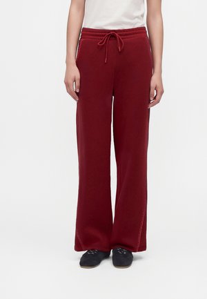 Modelo con pantalones burdeos de pernera ancha y cordón ajustable, con detalles de costuras laterales, un top blanco y zapatos negros.