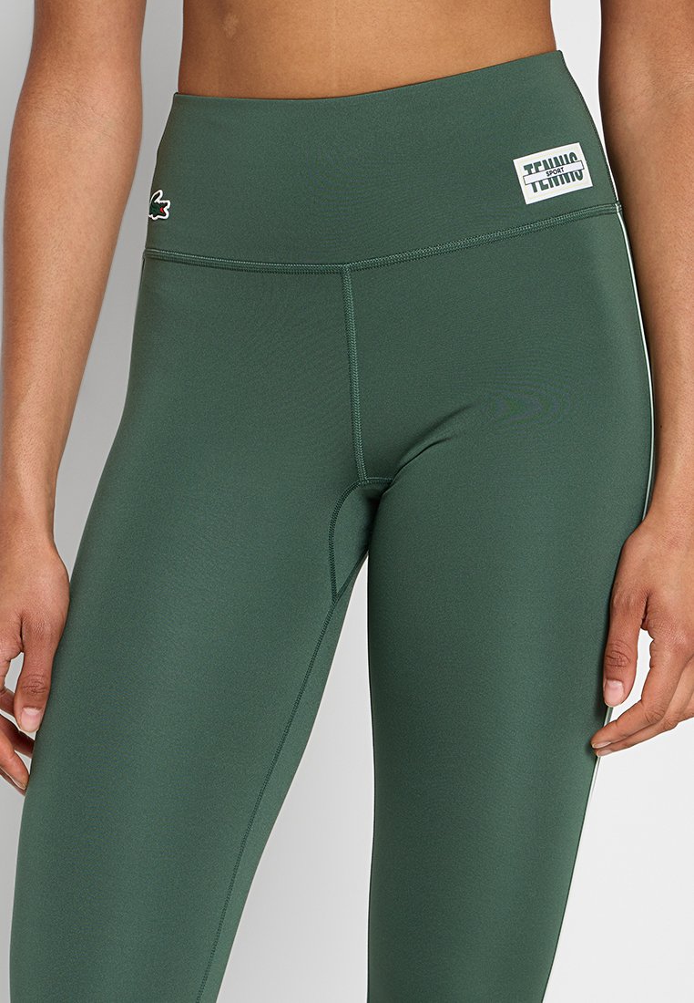 Leggings neri scuri a vita alta realizzati in materiale liscio e elasticizzato. Presentano cuciture piatte e un piccolo etichetta con logo vicino alla vita.