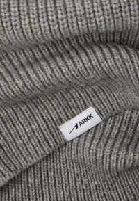 Gorro de punto gris con textura acanalada, diseño con doblez y una etiqueta blanca con "ARKK" cosida en el lateral.