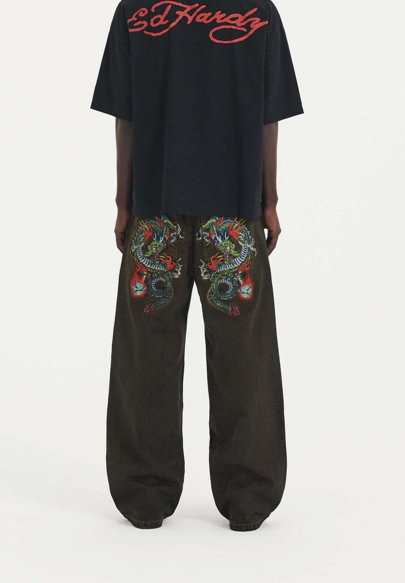 Camiseta negra de corte oversized con el logo rojo de "Ed Hardy", combinada con pantalones holgados oscuros que presentan bordados coloridos de dragones en la parte trasera.