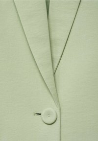 Tissu de blazer vert clair en gros plan montrant les revers et un seul bouton recouvert avec détail de boutonnière.