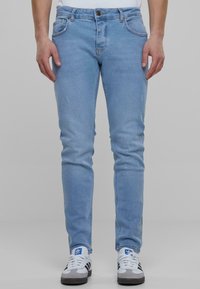 Világoskék, slim fit farmernadrág, kopott részletekkel, cipzáros zárással és elülső zsebekkel, szürke és fehér sportcipőkkel párosítva.