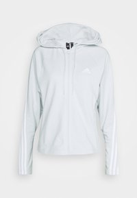 Sweat à capuche zippé blanc Adidas avec capuche, manches longues ornées de trois bandes et logo Adidas sur la poitrine.