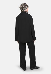 Zwarte oversized shirt met lange mouwen, gecombineerd met zwarte loszittende broek. Accessoires zijn onder andere een gestructureerde zwart-geel hoofddoek.