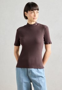 Braunes, geripptes Kurzarmoberteil mit hohem Hals und tailliertem Schnitt; zeichnet sich durch subtile Nähdetails am Kragen aus; glatte Textur.