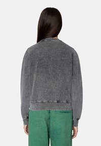 Grey denim jacket with a relaxed fit, ribbed cuffs, and hem. Back view shows a simple design, no visible patterns or logos. Paired with green pants.