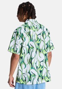 Πουκάμισο με κοντά μανίκια, με λευκή βάση και πράσινα και μαύρα αφηρημένα μοτίβα φλόγας. Υφασμάτινη υφή, άνετη εφαρμογή, γιακάς με κουμπιά.
