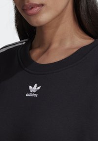 Zwarte crewneck sweatshirt gemaakt van katoen, met wit Adidas-logo en drie witte strepen op de schouders. Gladde textuur.