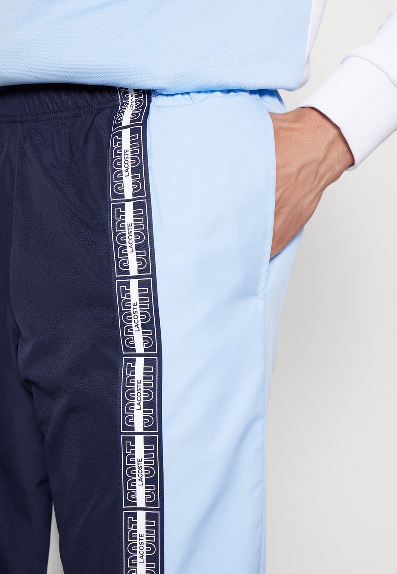 Pantalones de chándal en azul claro y marino con un acabado texturizado, que cuentan con un bolsillo lateral y rayas de marca a lo largo de la pierna.