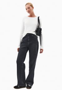 Biała koszula z długim rękawem, ciemne dżinsy z wysokim stanem, czarna torba i czarne trampki. Gładki materiał, luźny krój, szerokie nogawki, minimalne detale.