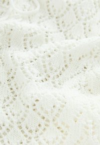 Tissu tricoté blanc avec un motif ajouré et des détails texturés. Le matériau semble doux et léger, adapté aux temps plus chauds.