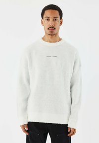 Witte fuzzy sweater gemaakt van zacht materiaal, met een geribbelde kraag en zoom. Inclusief geborduurde tekst "PROJECT X PARIS" op de borst.