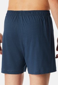 Marineblaue Muster-Badehosen mit elastischem Bund, die ein geometrisches Design und eine weiche Textur aufweisen. Die Rückansicht zeigt die lockere Passform.