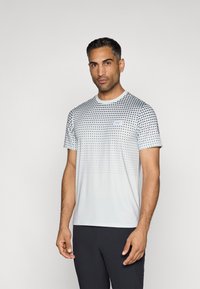 Atletisch T-shirt gemaakt van lichte stof, met een gradient van zwarte stippen op een lichtgrijze achtergrond, ronde halslijn, korte mouwen.