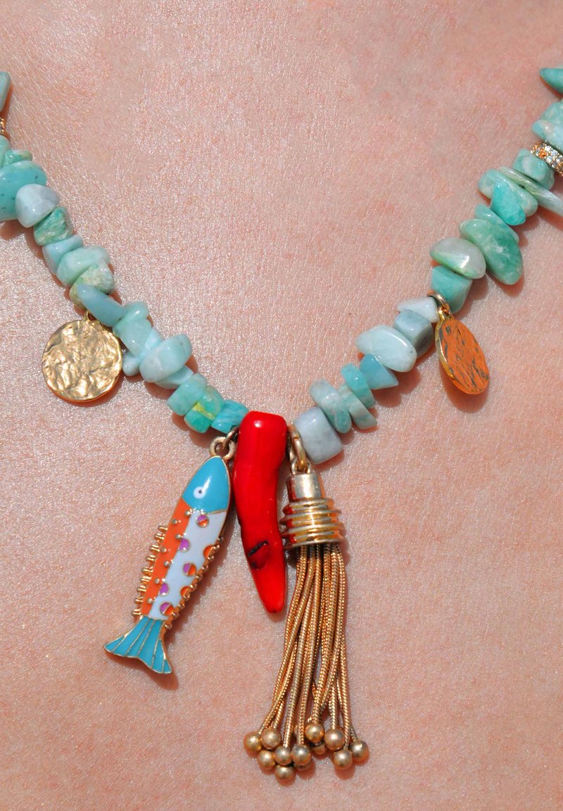 Le collier en pierre turquoise présente une pièce de monnaie dorée texturée, un piment rouge, un charme en forme de poisson avec des accents bleus et un gland doré. Des détails vifs et colorés.