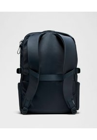 Juodas kuprinės modelis su paminkštintomis diržais, lygia tekstūra, dvigubomis šoninėmis kišenėmis ir minimalistiniu dizainu, kuriame yra užtrauktukai ir reguliuojamos detalės.