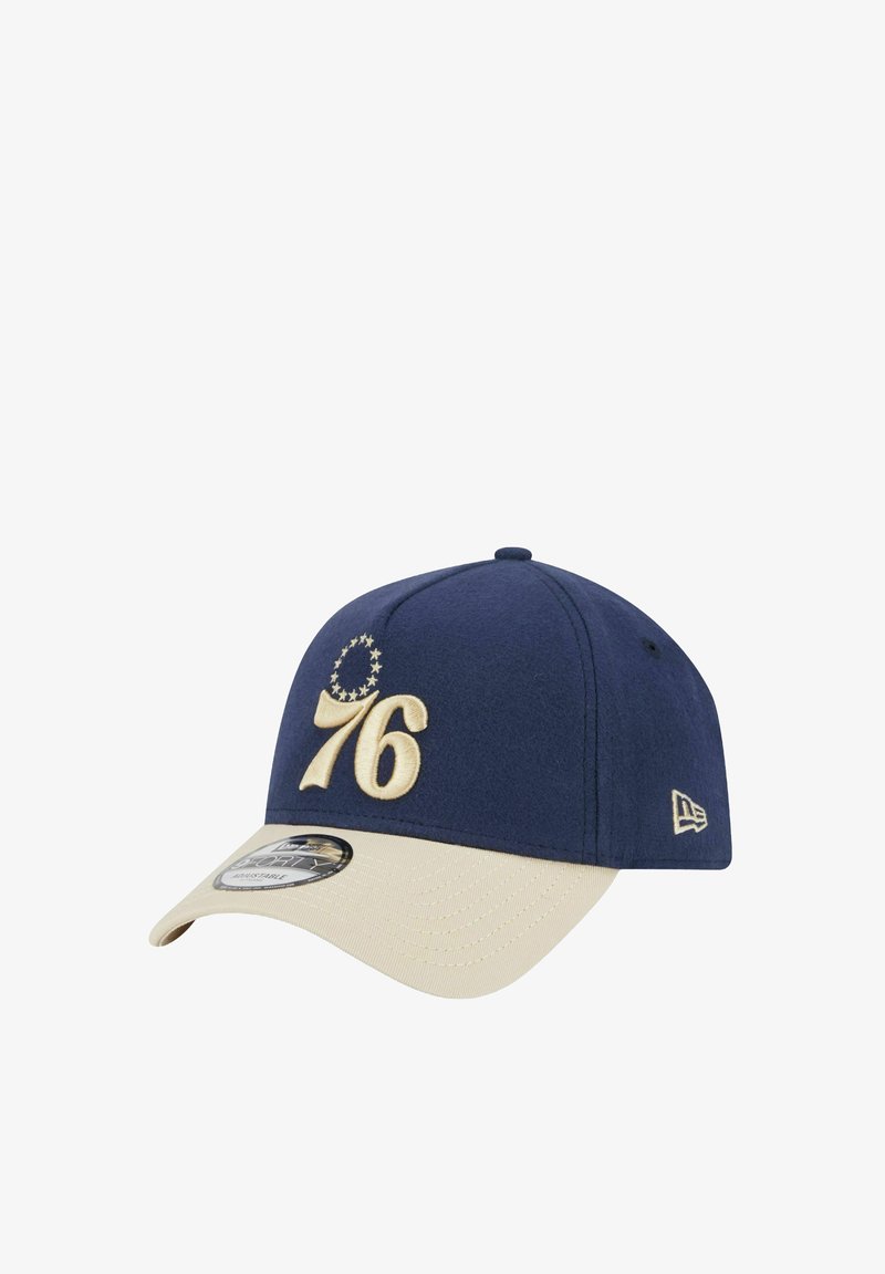 Marineblaue Baseballmütze mit beigem Schild, mit gestickter "76" und einem Sternenkreis-Design. Hergestellt aus weichem Stoff, strukturierte Form.