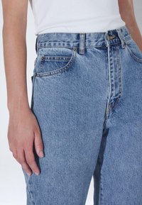 Světle modré džínové kalhoty s vysokým pasem, pěti kapsami a jemným vyblednutím na stehnech. Viditelné kovové doplňky a prošité švy.
