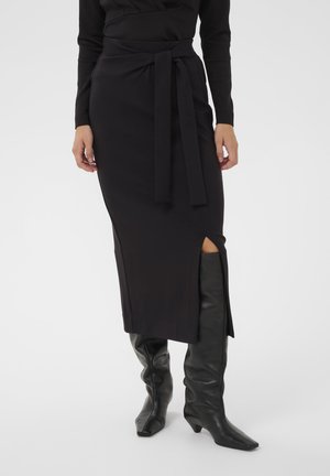 Sort midi-nederdel med en sideslids og et bundet stofbælte. Glat tekstur, tætsiddende design, parret med knæhøje sorte læderstøvler.