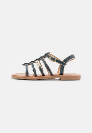 Sandali con cinturini in stampa serpente blu scuro con suola in pelle color tan. Presentano una cinghia alla caviglia regolabile con fibbia dorata e cinque cinturini verticali.