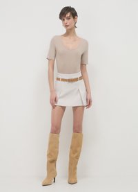 Body beige con scollo a barca, gonna mini plissettata bianca con cintura color sabbia e stivali alti in suede color sabbia con tacco. Design semplice e moderno.