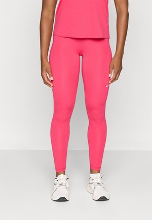 Rózsaszín sport leggings, elasztikus anyagból, sima tapintással és egy kis fehér logóval a derékpánt közelében, fehér sportcipővel párosítva.